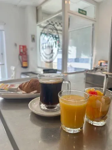 Desayuno con café, zumo, fruta y croissant en un mostrador de plata de una cafetería.