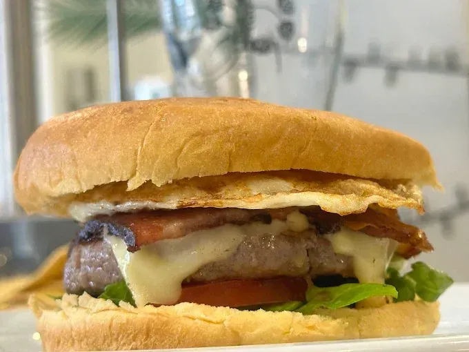 Hamburguesa con huevo frito, tocino, tomate y queso en pan.