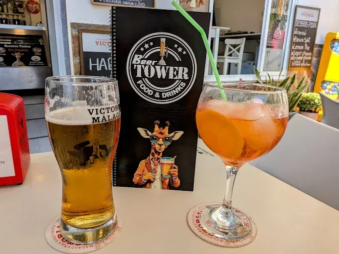 Cerveza y un cóctel de naranja sobre una mesa de bar. Un menú con una jirafa al fondo.
