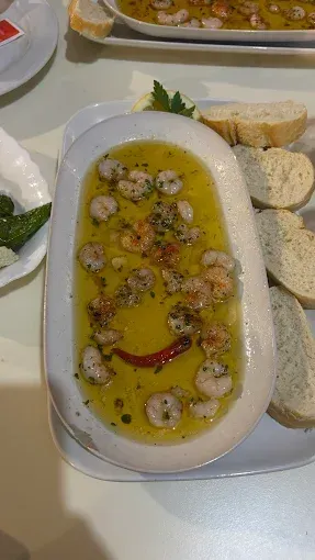 Camarones en aceite de oliva con pan en una bandeja blanca. Un pimiento rojo decora el plato, simulando una carita feliz.