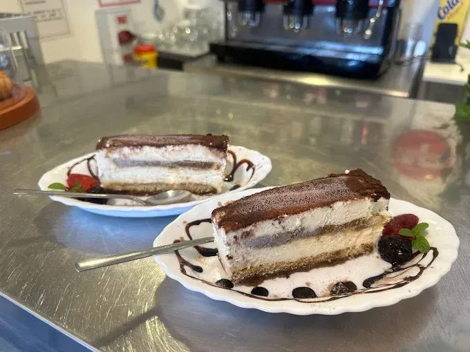 Dos rebanadas de tiramisú en platos blancos, rociadas con salsa de chocolate, sobre un mostrador de metal.