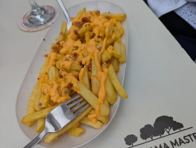 Papas fritas con salsa de queso y naranja y trocitos de tocino en un plato blanco con un tenedor.