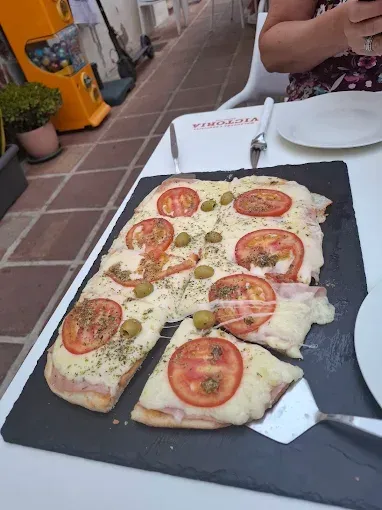 Pizza con tomates y aceitunas en una bandeja negra en la mesa de un restaurante.
