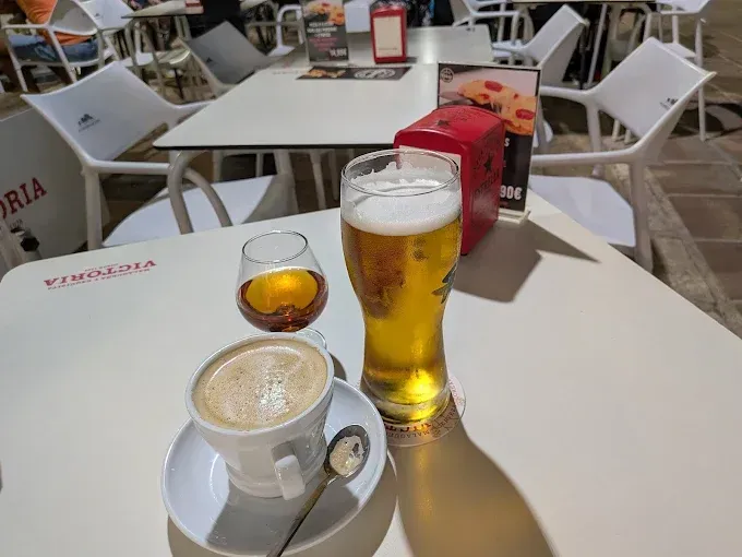 Mesa con café, cerveza y licor, al aire libre en una cafetería. Sillas, mesa y decoración blancas.