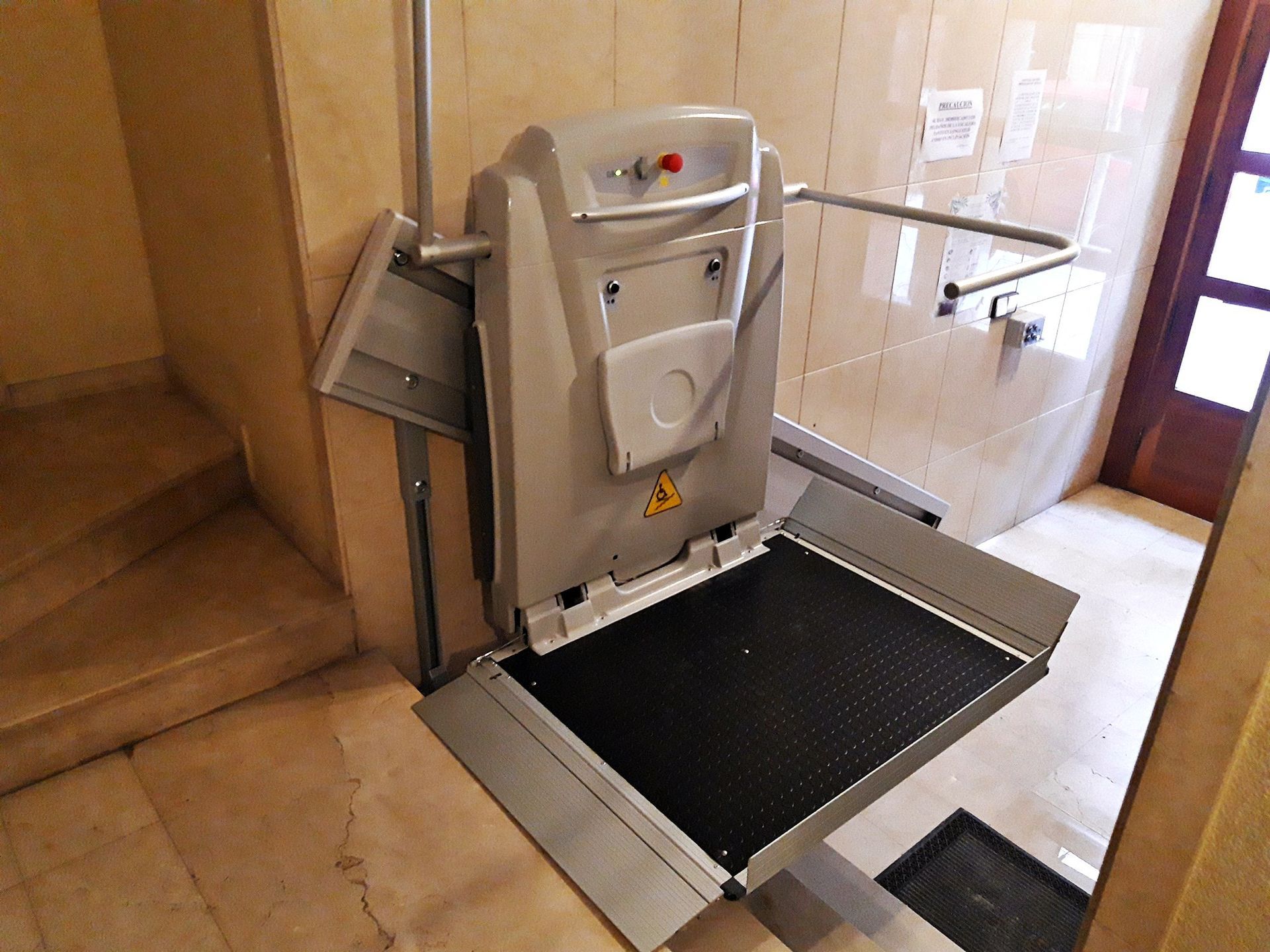 Hay un elevador para sillas de ruedas en un pasillo al lado de las escaleras.