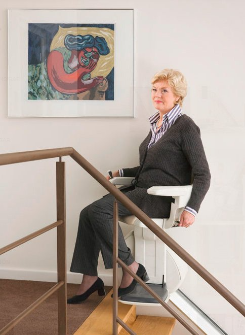 Una mujer está sentada en un salvaescaleras con un cuadro en la pared detrás de ella.