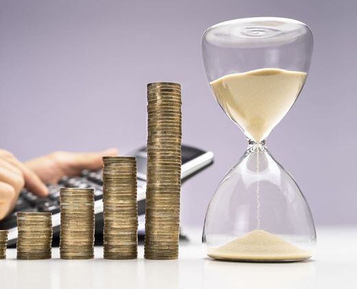 Una persona está escribiendo en un teclado junto a pilas de monedas y un reloj de arena.