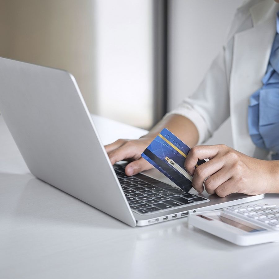 Una mujer sostiene una tarjeta de crédito mientras usa una computadora portátil.