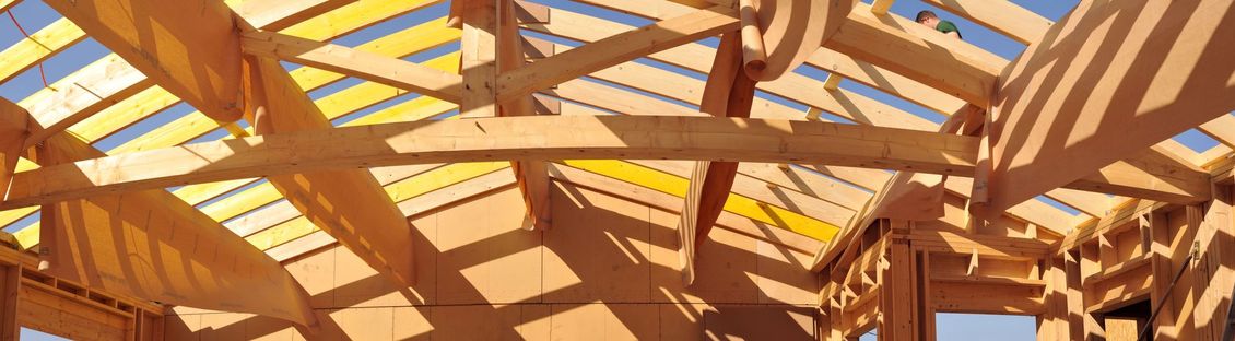 Charpente de toit en bois en construction sur fond de ciel bleu éclatant, le soleil projetant des ombres nettes.