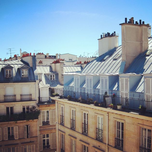 Toits de Paris aux toits mansardés gris, cheminées et immeubles couleur crème baignés de soleil.