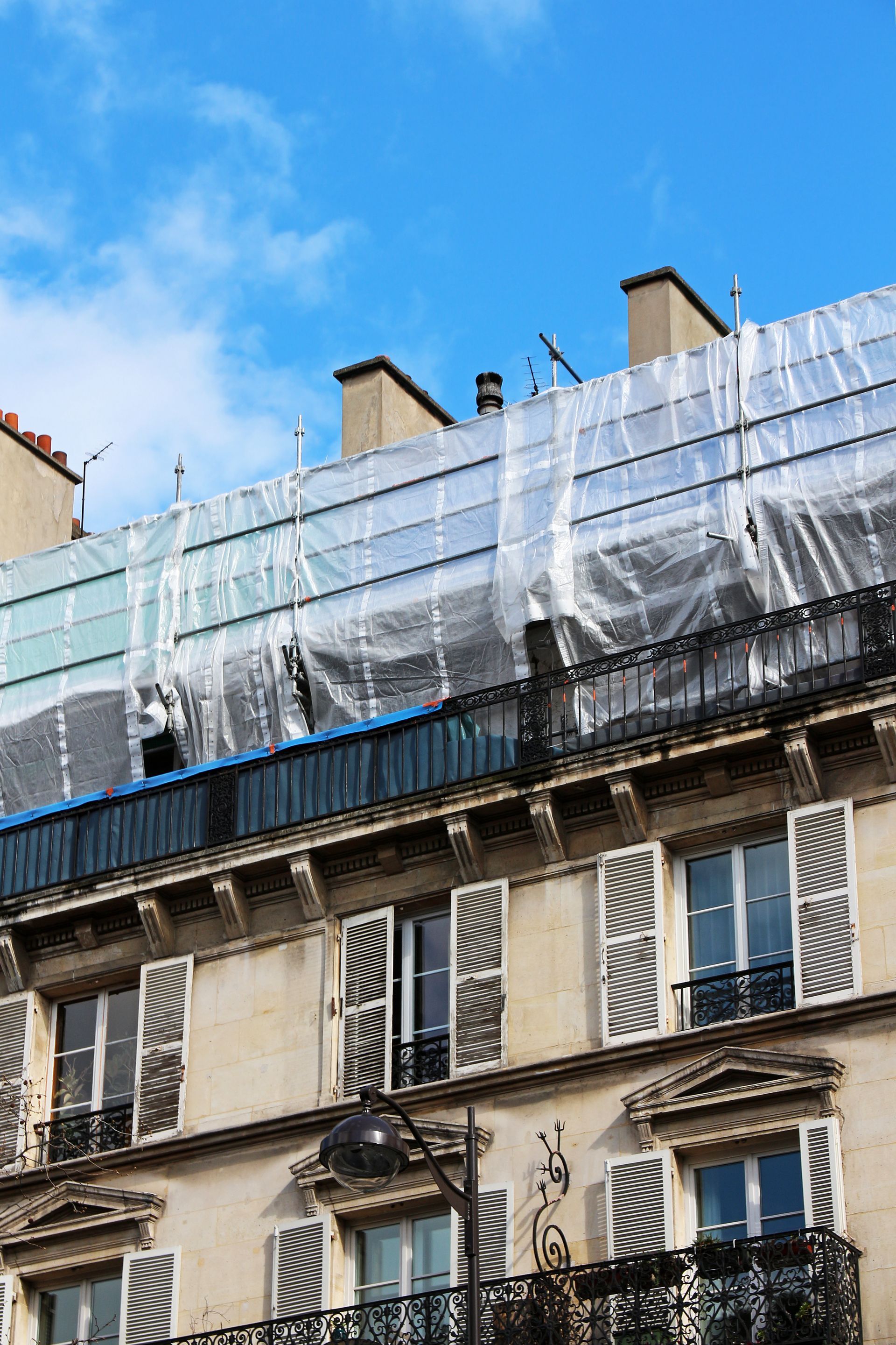 Immeuble d'appartements avec échafaudages sur le toit recouverts d'une bâche blanche sous un ciel bleu