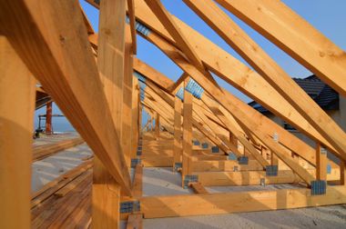 Charpente de toit en bois en construction sur un chantier, se détachant sur un ciel bleu clair.
