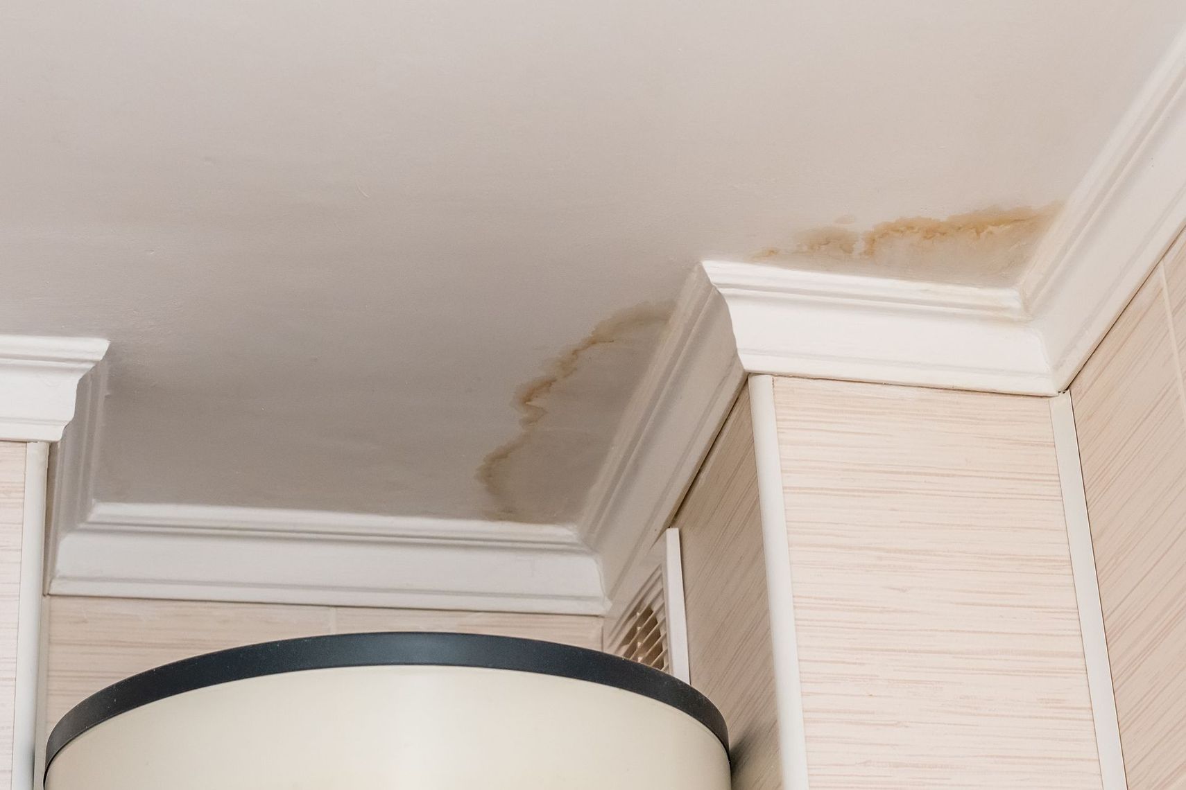 Plafond taché d'eau au-dessus d'une lampe et d'armoires blanches dans une pièce