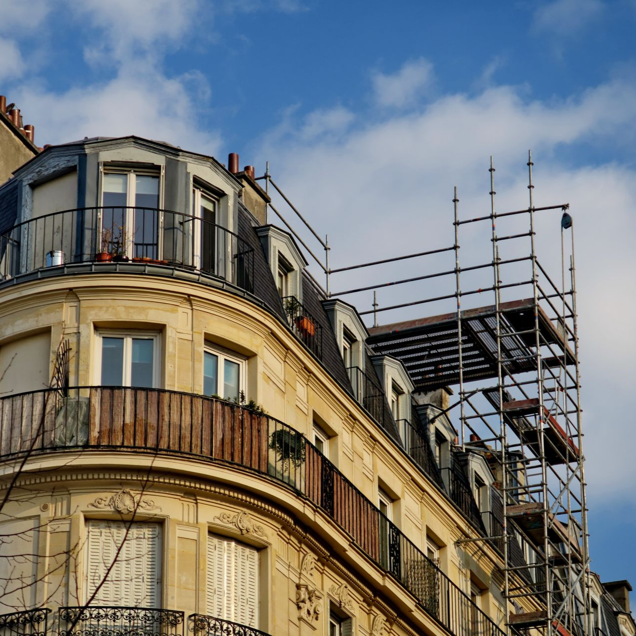 Bâtiment historique beige avec balcons et échafaudages se détachant sur un ciel bleu