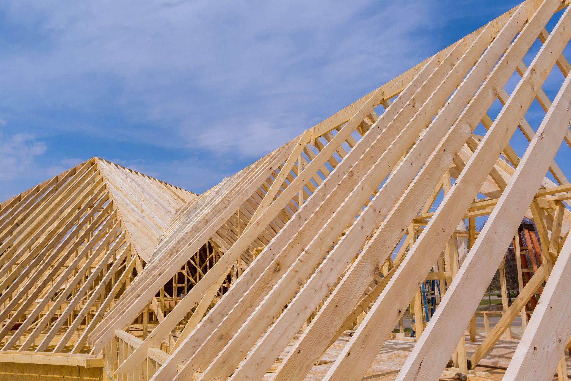 Charpente de toit en bois en construction sur fond de ciel bleu, avec la structure d'une maison en arrière-plan.