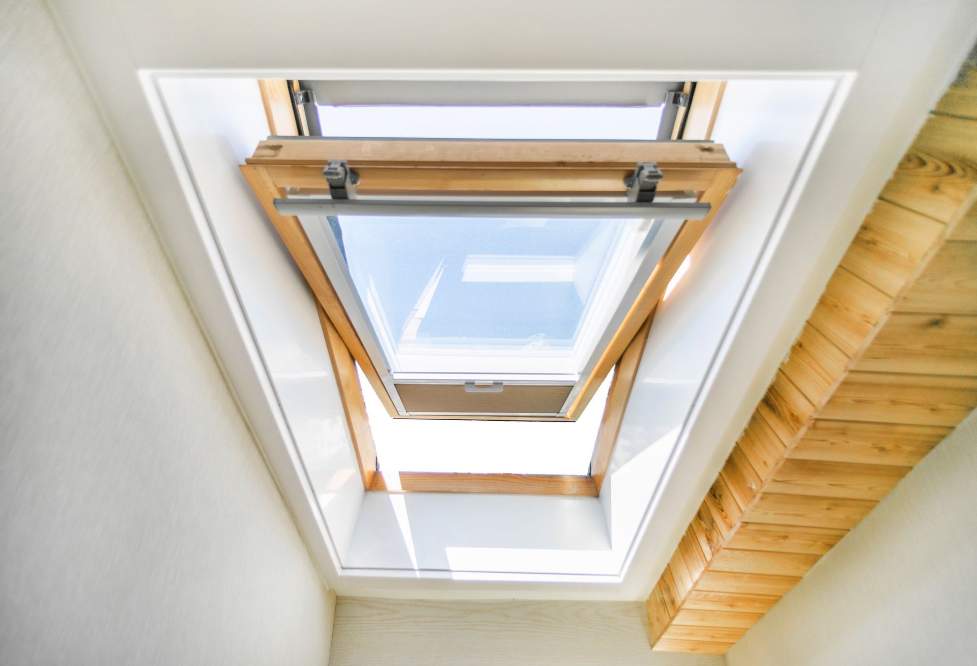 Fenêtre de toit ouverte dans un plafond blanc à cadre en bois, laissant entrer une lumière naturelle abondante.