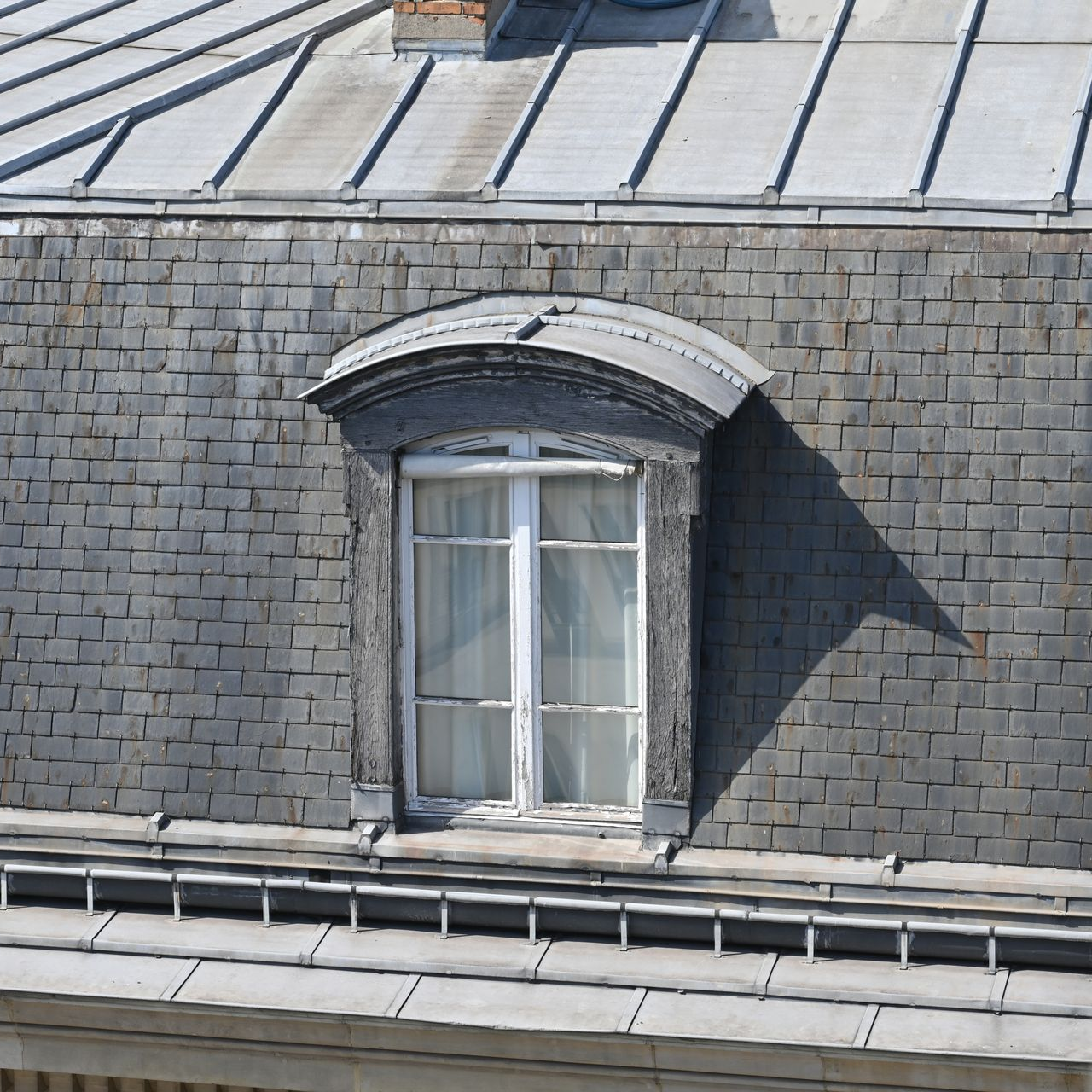 Lucarne en pierre sur un toit d'ardoise grise sous un soleil éclatant