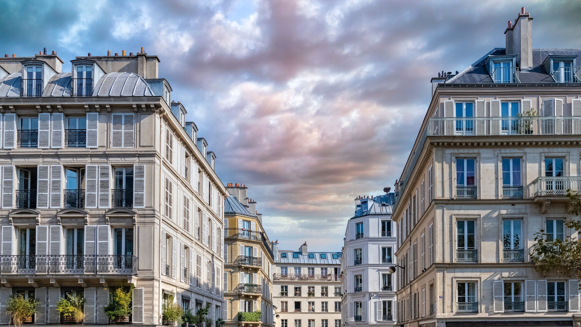 Des immeubles de style parisien bordent une rue sous un ciel nuageux