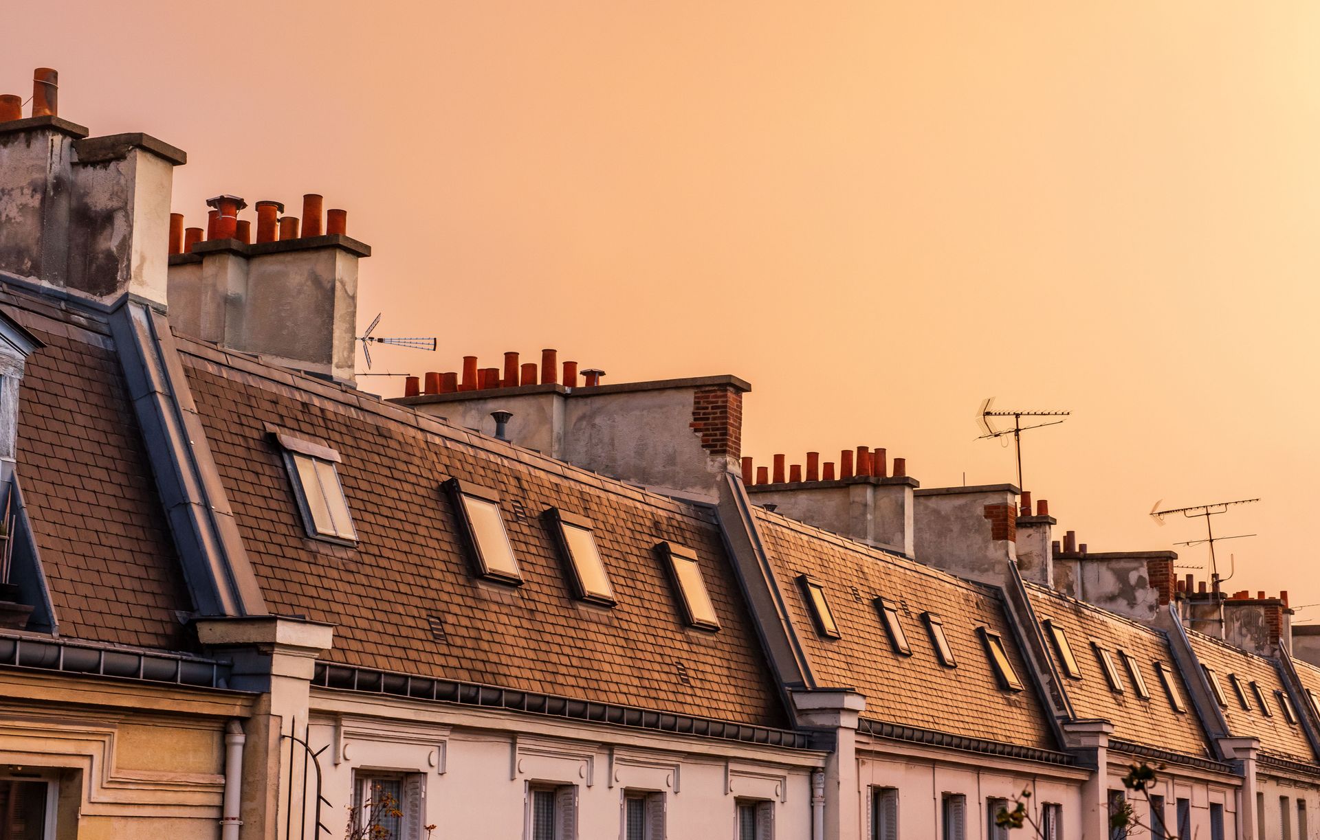 Rangée ensoleillée de vieux toits européens avec des lucarnes sous un ciel orangé