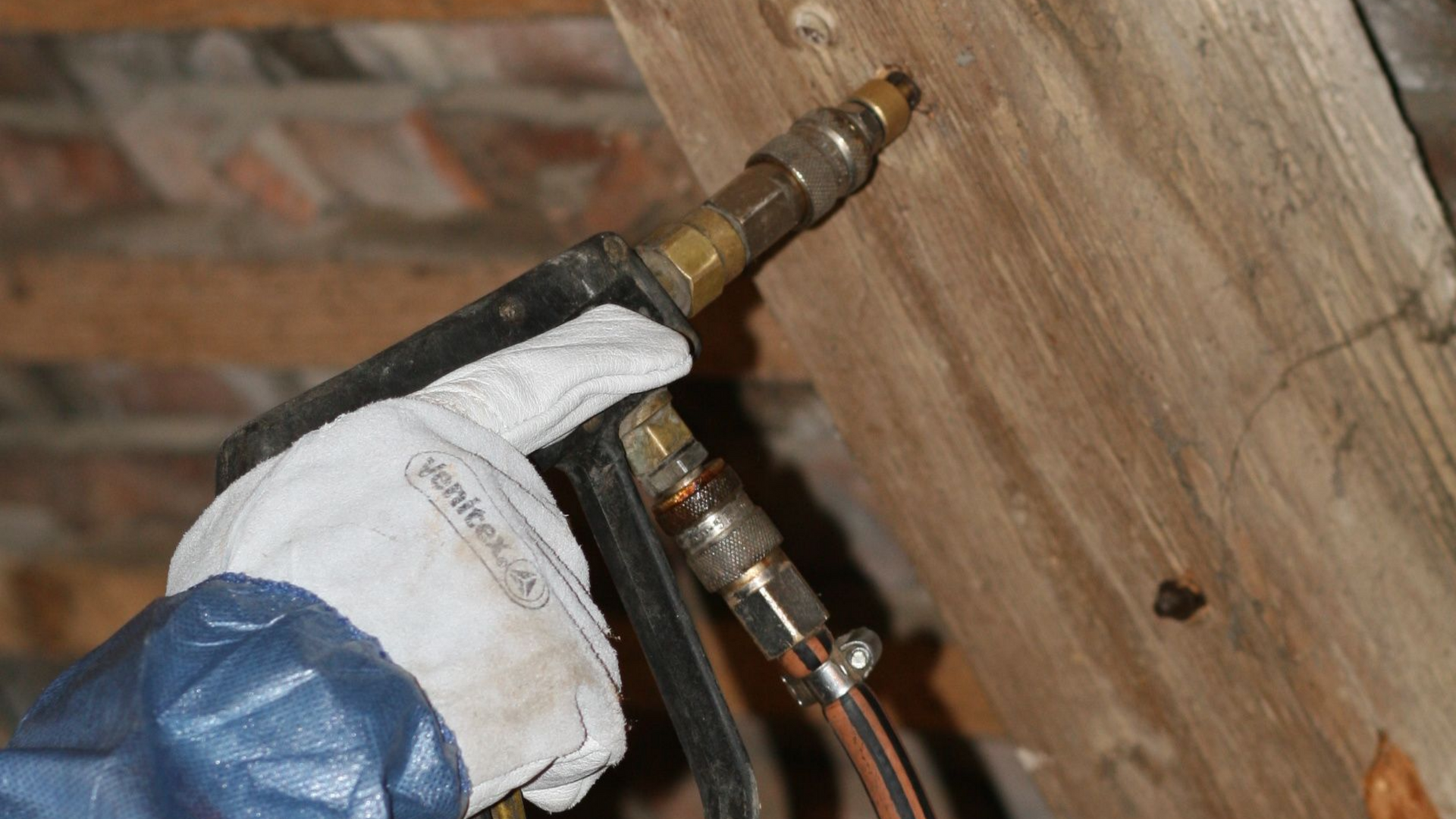 Main gantée manipulant un raccord sur des tuyaux de cuivre contre une surface en bois