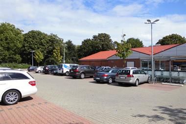 Auf einem Parkplatz vor einem Gebäude stehen viele Autos.