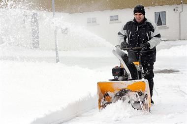 Ein Mann benutzt eine Schneefräse, um Schnee vom Gehweg zu entfernen.