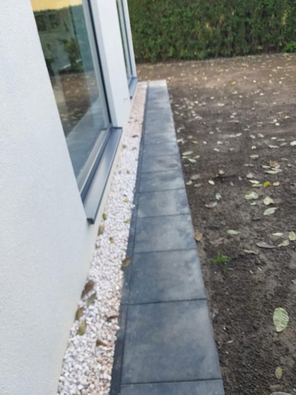 Ein Gehweg neben einem Haus mit Kies und einem Fenster.