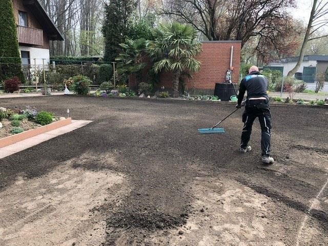 Ein Mann harkt Erde in einer Einfahrt vor einem Haus.
