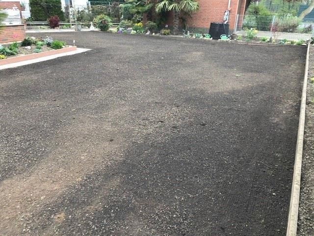 Eine schwarze Asphaltauffahrt mit einem Backsteingebäude im Hintergrund.