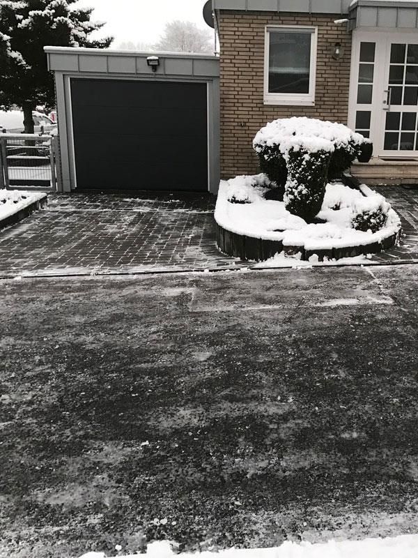 Ein Schwarzweißfoto einer verschneiten Auffahrt vor einem Haus