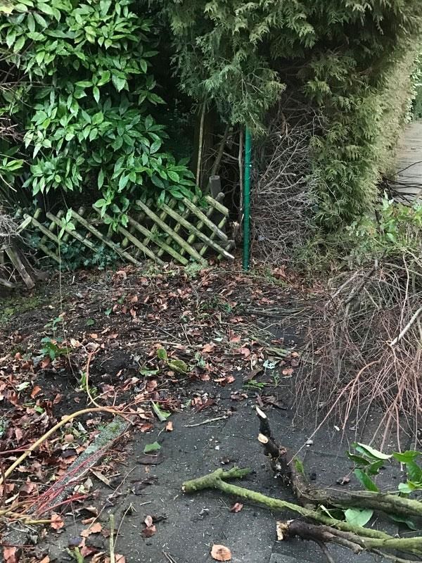 Ein Holzzaun steht am Straßenrand neben einem Haufen Äste.