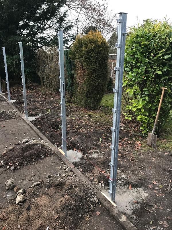 In einem Garten wird mit einer Schaufel im Dreck ein Zaun gebaut.