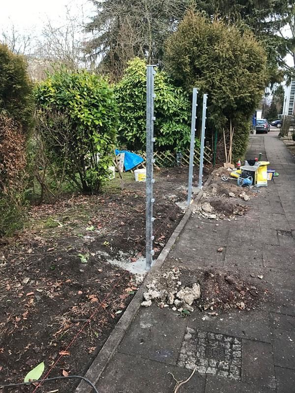 In einem Garten neben einem Gehweg wird ein Zaun gebaut.