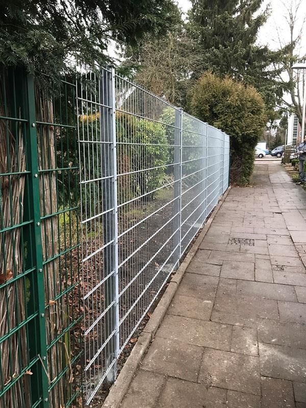 Ein weiß-grüner Zaun entlang eines Gehwegs.