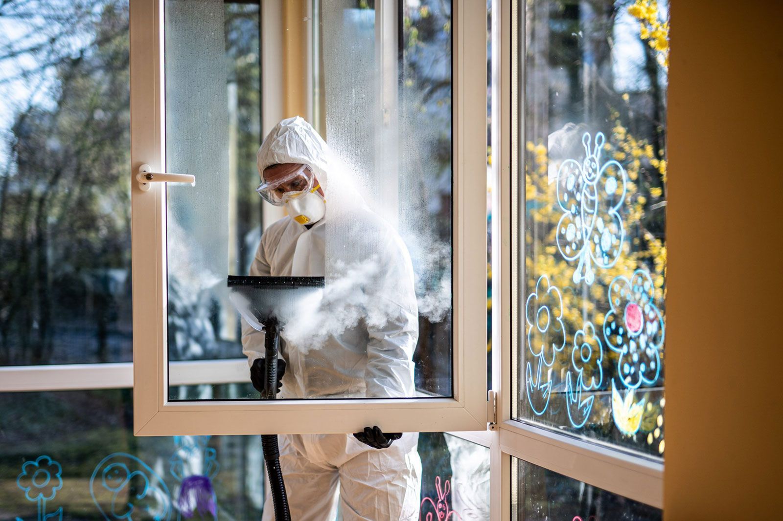 Ein Mann im Schutzanzug spritzt mit einem Staubsauger ein Fenster ab.