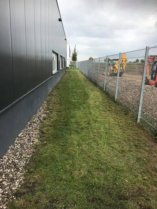 Ein Zaun umgibt ein üppiges grünes Feld neben einem Gebäude.