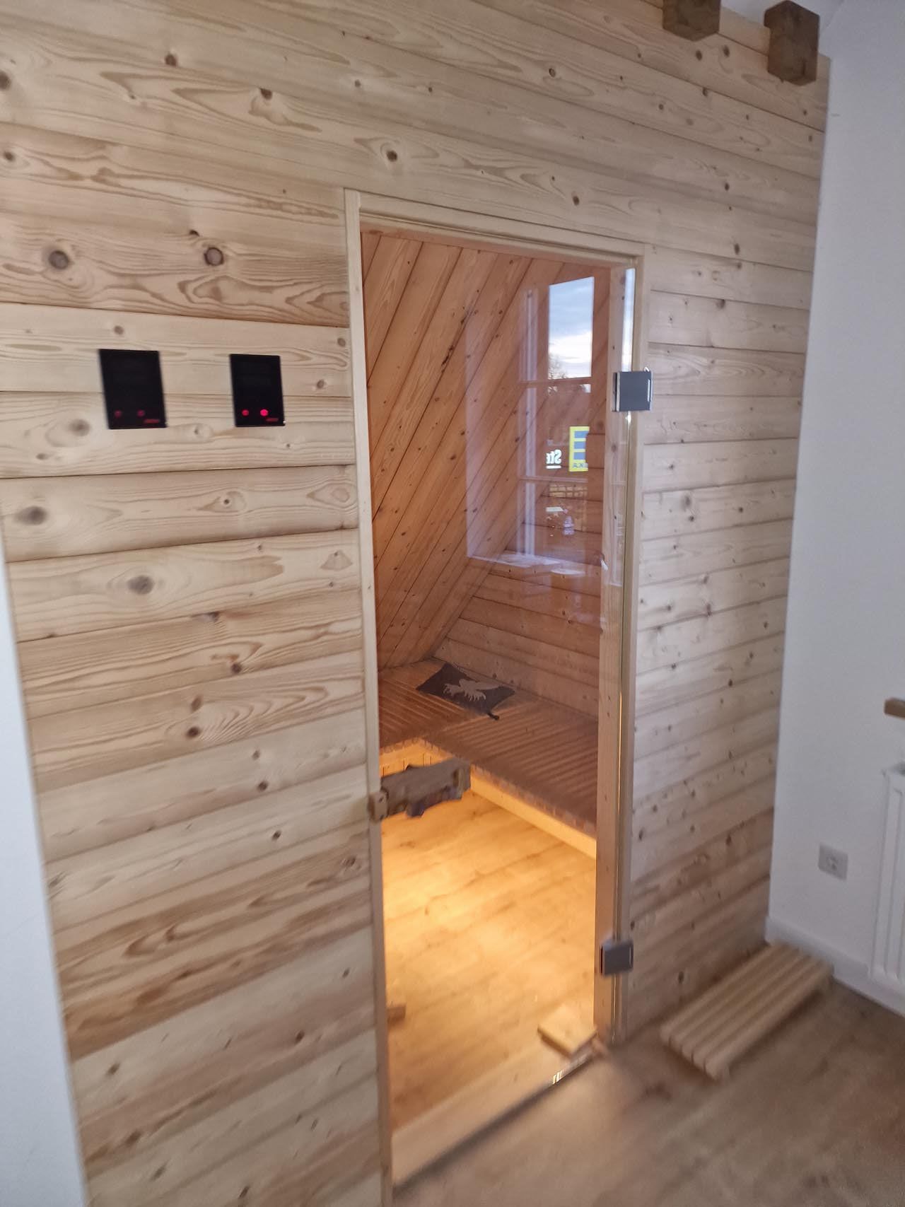 Ein Saunaraum mit einer Holzwand und einer Glastür von Hubert Uppenkamp GmbH