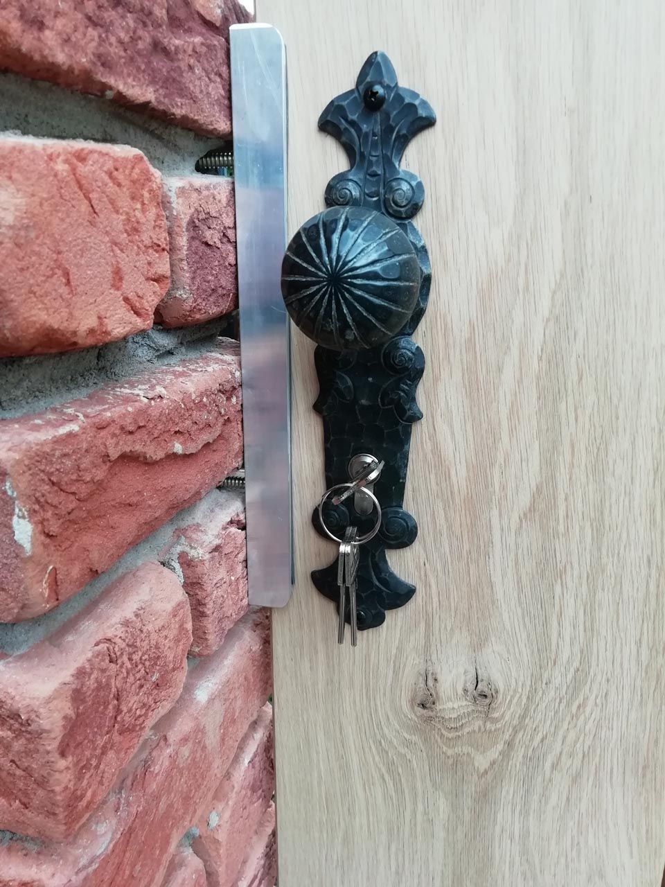 An einer Holztür neben einer Ziegelwand hängt ein Schlüssel.