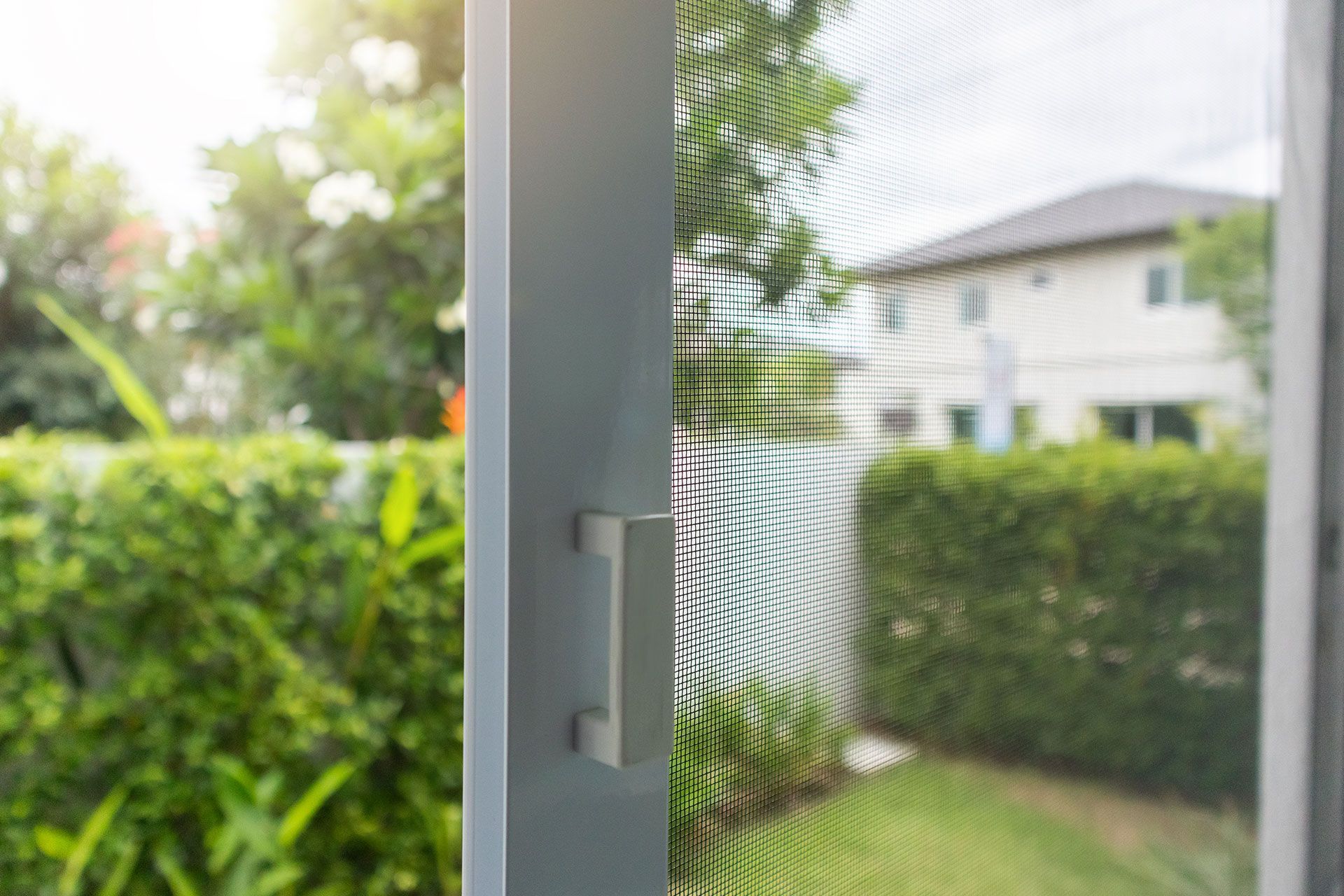Eine Schiebetür mit Fliegengitter öffnet sich zu einem Hinterhof mit einem Haus im Hintergrund.