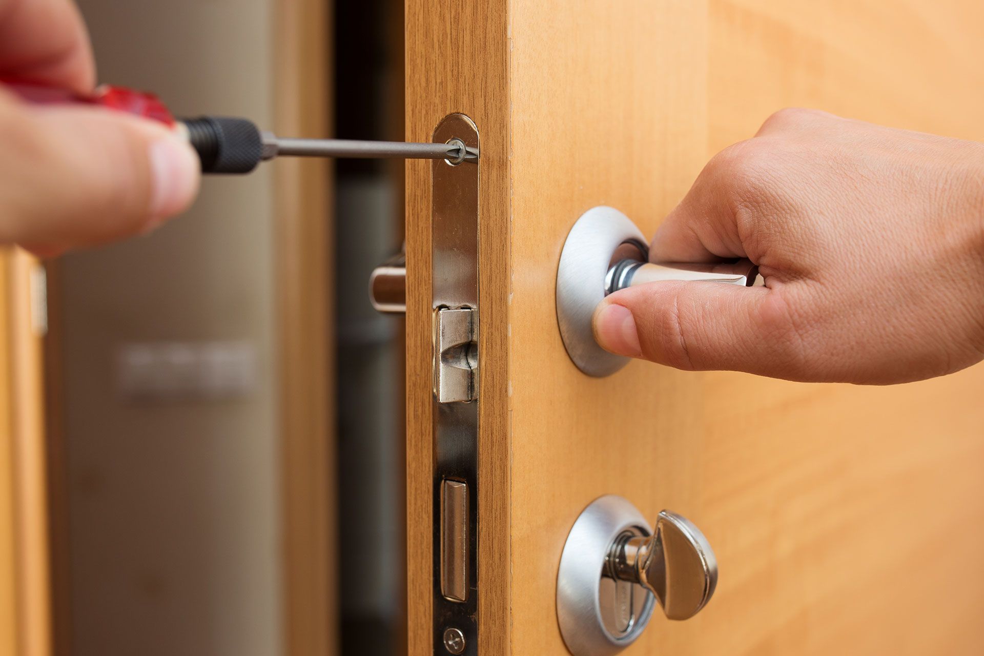 Eine Person repariert eine Schließanlage einer Tür mit einem Schraubenzieher.