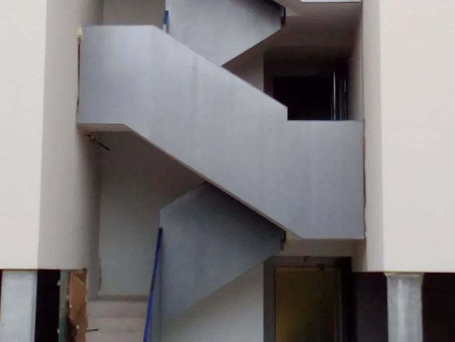 Escalera de hormigón en un patio estrecho con paredes grises y pasamanos azul.