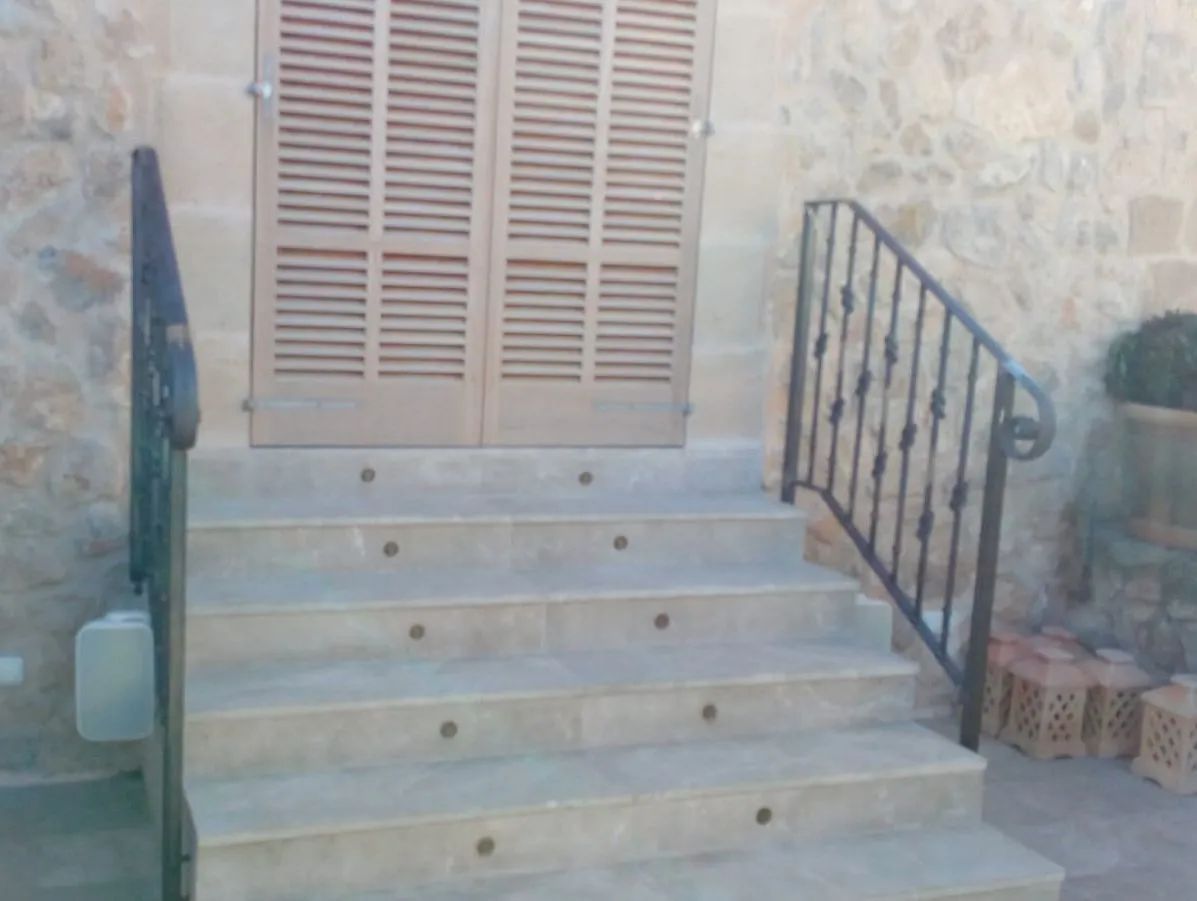 Escalones de piedra conducen a una puerta cerrada con contraventanas, con pasamanos de metal a ambos lados.