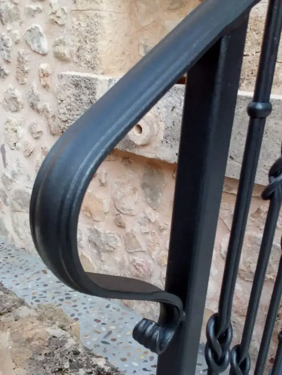Barandilla de escalera de metal negro contra una pared de piedra.