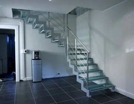 Interior moderno con suelo de baldosas grises y escalera flotante blanca con barandilla metálica.