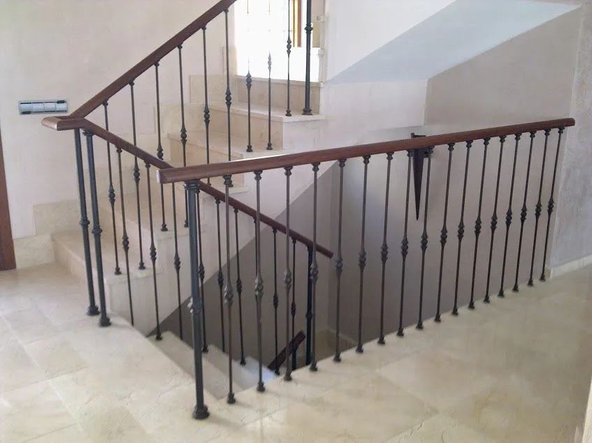 Escalera interior con escalones de piedra beige y barandilla de metal oscuro.