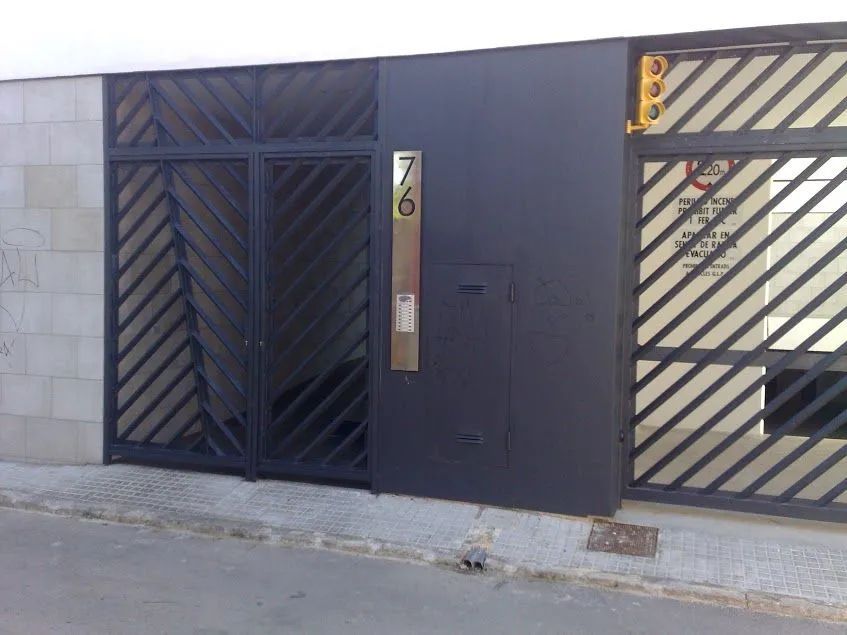 Puerta y portal de metal negro en un muro de hormigón, con una puerta de garaje a rayas al lado.