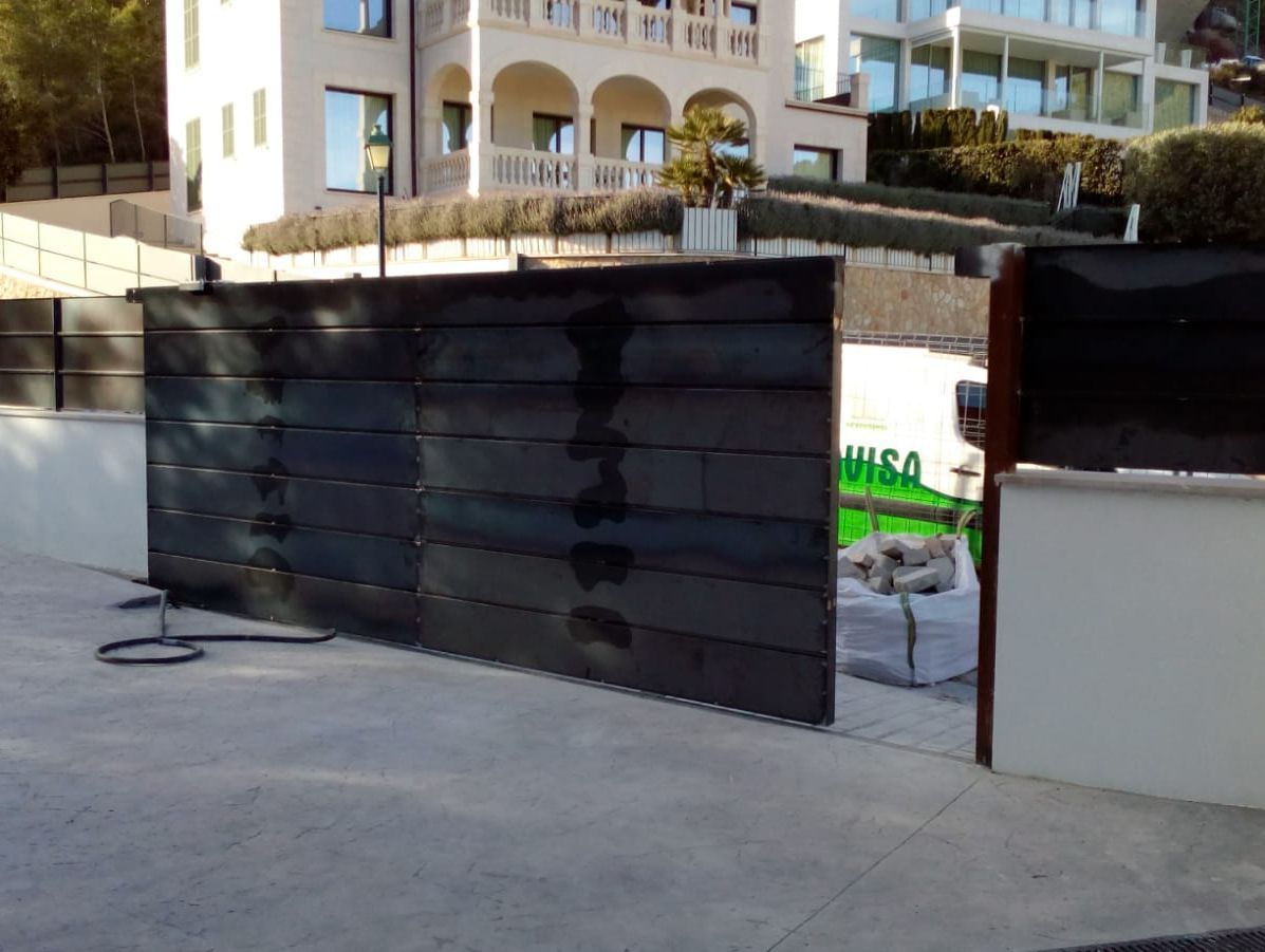 Puertas de madera negra en la entrada de un edificio con una pared blanca y balcones de apartamentos al fondo.
