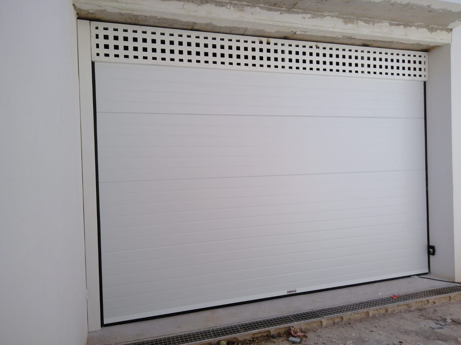 Puerta de garaje metálica blanca cerrada debajo de un panel de ventilación perforado.