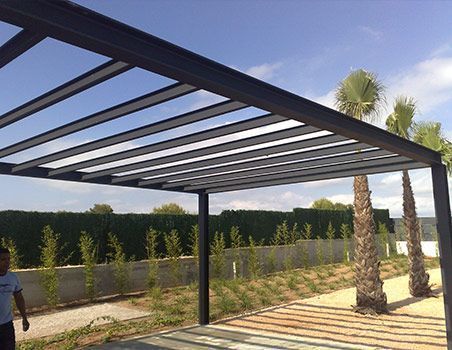 Pérgola moderna con vigas oscuras sobre un sendero soleado en el patio trasero y una palmera.