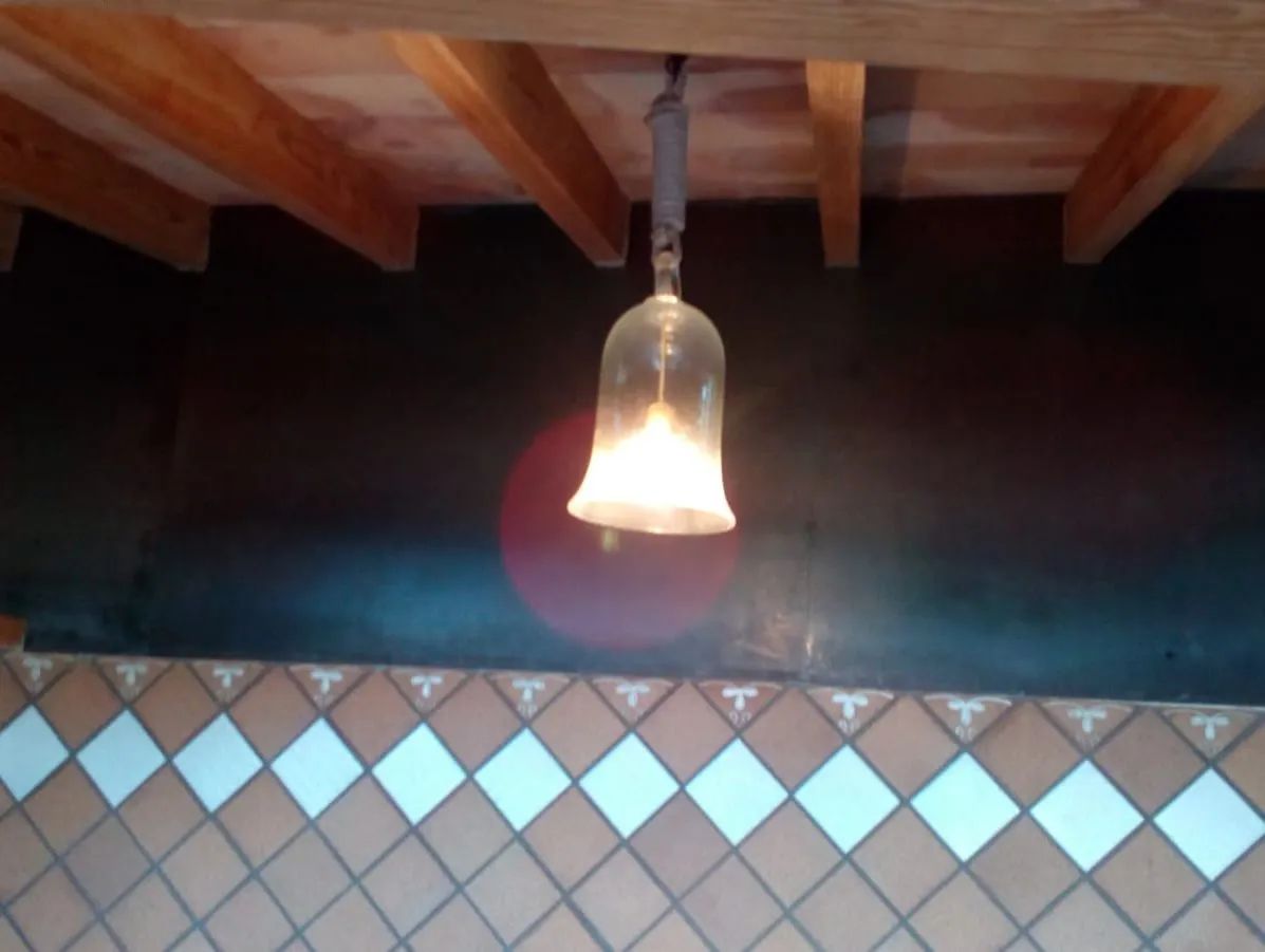 Una lámpara colgante sobre una pared alicatada con vigas de madera en el techo.